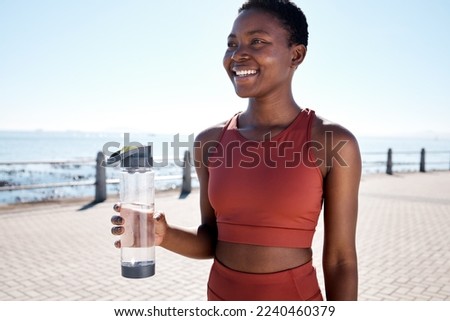 Fitness, water and black woman runner at beach for training, wellness and cardio by ocean, smile and happy. Exercise, drinking water and woman relax after running, workout and walk with hydration Royalty-Free Stock Photo #2240460379