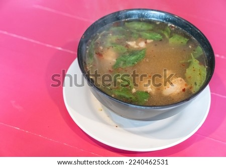 Traditional thai spicy Tom yum soup with chicken served in black bowl and on white dish with wooden pink table