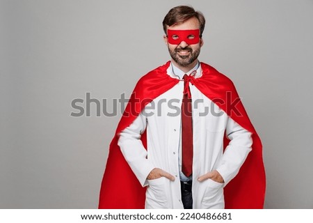 Male doctor man wears white medical gown suit work in hospital wear red super hero coat stand akimbo hands on waist isolated on plain grey color background studio portrait. Healthcare medicine concept
