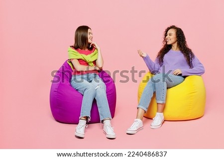 Full body young two friends positive happy fun cheerful women 20s wears green purple shirts together sit in bag chair talk speak isolated on pastel plain light pink color background studio portrait Royalty-Free Stock Photo #2240486837