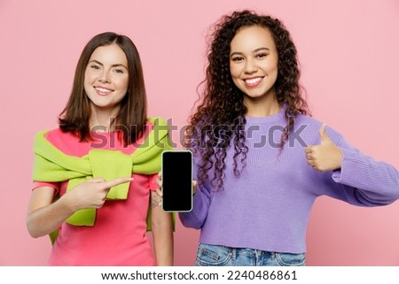 Young two friends fun women wears green purple shirts together hold in hand use mobile cell phone with blank screen workspace area show thumb up isolated on pastel plain light pink color background