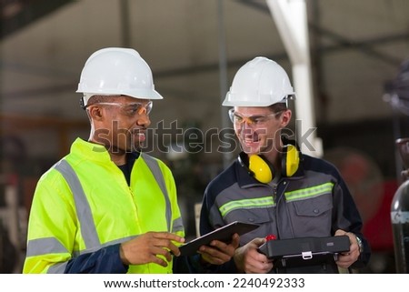 Two male engineer workers discuss and holding digital tablet working in the industry factory