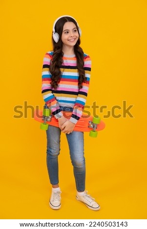 Teenagers lifestyle, casual youth culture. Teen girl with skateboard and headphone over isolated yellow studio background. Cool modern teenager in stylish clothes. Happy teenager.