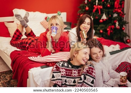 Girls pajamas party near Christmas tree with drinks and sparkles. Best happy friends hanging out, having fun, laughing