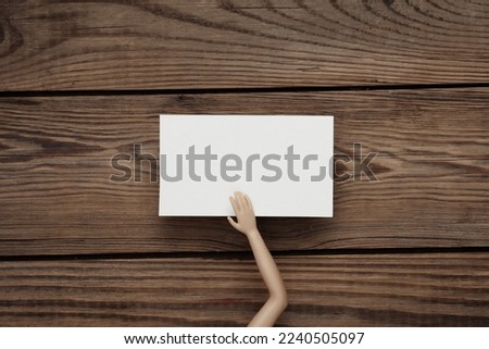 White Blank business card for corporate identity in doll hand on wooden background. Creative mockup