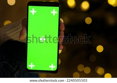 Hand holding Chroma Key Green Screen in vertical Position without touching, swiping at Christmas evening. Using phone with green mock-up, surfing Internet, watching content videos, apps