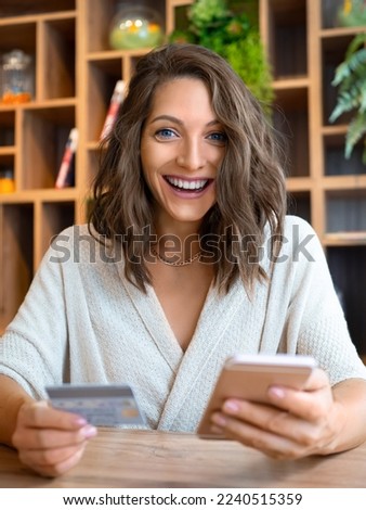 Vertical photo of a happy smiling young woman with a smartphone and a credit card. She smiles happily and looks into the camera. Online shopping and sales concept.