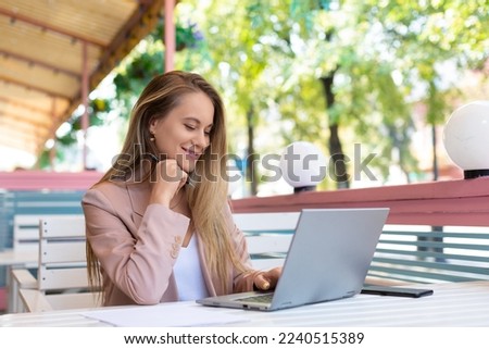 Woman in working in front of laptop monitor at summer cafe. She looking at laptop monitor and smiling. Modern technology in every day life concept.