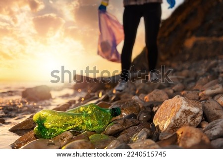 Pollution recycling and social problems. A volunteer walks along a pebble beach and collects plastic bottle. Low angle view. The concept of cleaning coastal area from garbage.