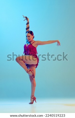 Solo. Portrait of young graceful flexible woman dancing ballroom dance without partner isolated on blue background in neon light. Concept of art, timeless, beauty, music, style