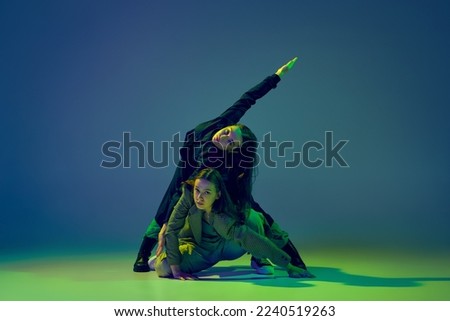Weird. Stylish young girls in casual clothes dancing experimental style dance over gradient blue-green background at dance hall in neon light. Youth culture, contemporary dance, fashion, action.