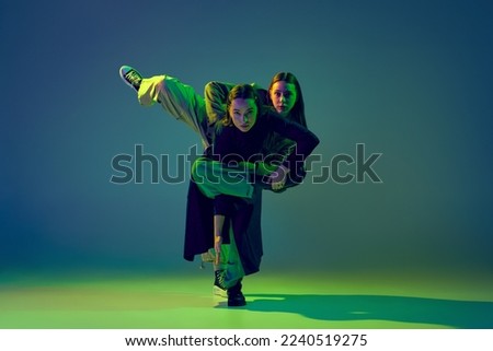 Stylish young girls dancing casual clothes dancing experimental style dance over gradient blue-green background at dance hall in neon light. Youth culture, contemporary dance, fashion, action. Royalty-Free Stock Photo #2240519275