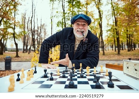 Portrait of senior man playing chess in the park on a daytime in fall. Cheerful discussion. Concept of leisure activity, friendship, sport, autumn season, game, entertainment, old generation