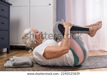 Woman lying on yoga mat doing apanasana. Fit female relaxing on floor at home. Royalty-Free Stock Photo #2240525839