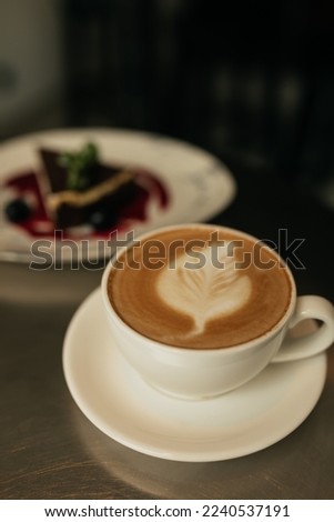 Photo of tasty cheesecake with cup of cappuccino in focus. Cup of coffee standing on silver table near plate with dessert.