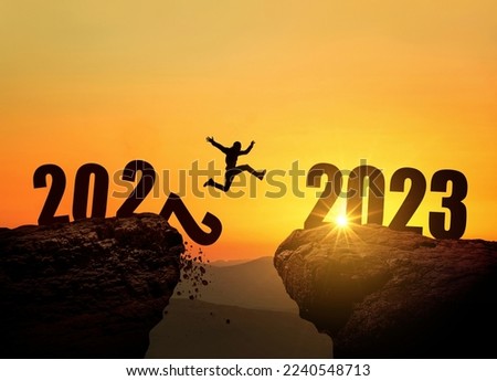 Man jumping on cliff 2023 over the precipice with stones at amazing sunset. New Year's concept. 2022 falls into the abyss. Welcome 2023. People enters the year 2023, creative idea.