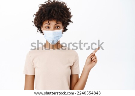 Girl in medical face mask, pointing finger at banner, showing text advertisement or copy space