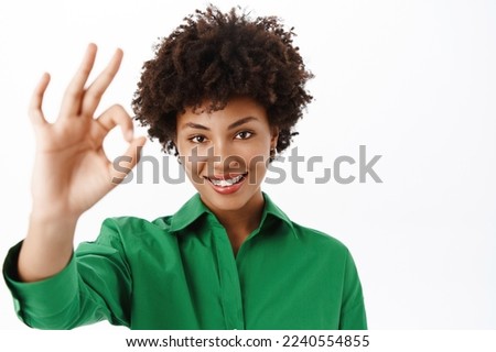 Portrait of young smiling Black girl, shows okay, ok sign in approval, agree with you, say yes, recommending product, white studio background