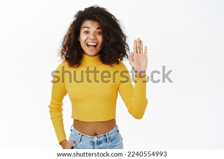 Friendly young african american woman saying hello, waving hand, say hi, greeting, welcome gesture, smiling happy, standing over white background