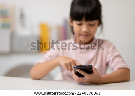 Cute little girl uses smartphone while sitting at the sofa in the living room. Child surfing the internet on mobile phone, browses through internet and watches cartoons online at home