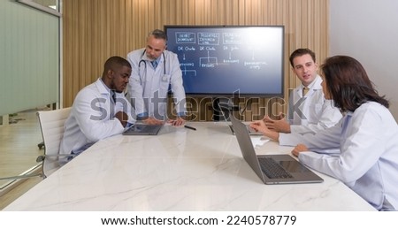 Group of doctors meeting in office with flat screen TV for presentation. Everyone has their own laptop computer. Royalty-Free Stock Photo #2240578779