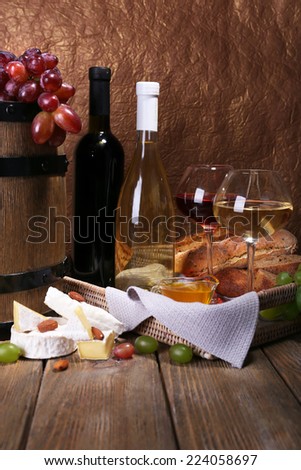Supper consisting of Camembert and Brie cheese, wine and grapes on napkin in basket and wine barrel on wooden table on brown background