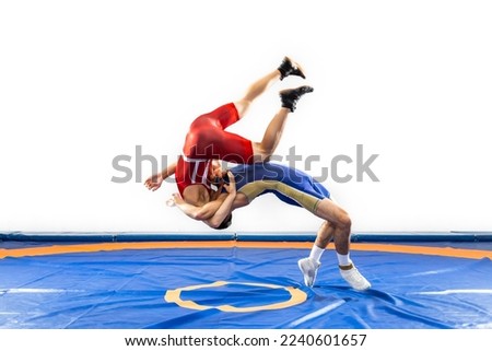 Two  strong men in blue and red wrestling tights are wrestlng and making a suplex wrestling on a yellow wrestling carpet Royalty-Free Stock Photo #2240601657