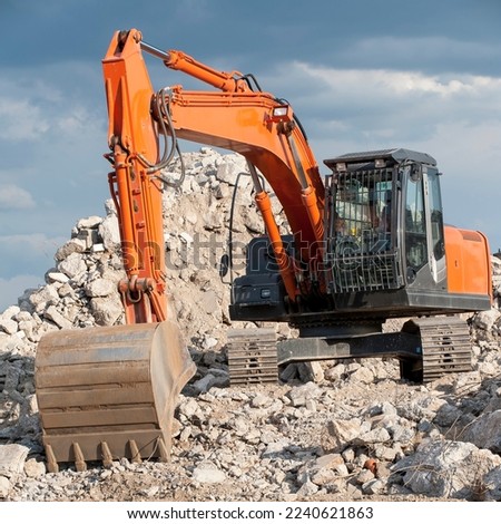 Square photo of an excavator with chain wheels and shovel standing on a pile of rubble without logos and other legal identifiers.