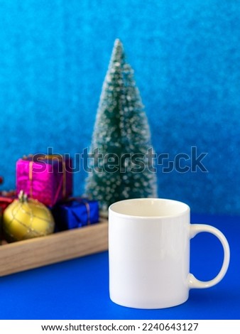 Christmas background with white mug mockup, blue glittering wall, and ornaments on blue navy desktop.