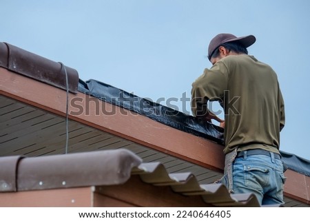 Black adhesive tape for hermetic joints of roofing materials, when mounting the roof, Tool for waterproofing on a background of roof.Asian worker installing bitumen foil on the roof.
