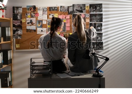 Smart detectives looking attentively at investigation board, evaluating clues, while sitting on the table. Copy space Royalty-Free Stock Photo #2240666249