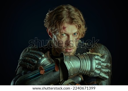 Portrait of a handsome medieval knight with scars on his face in armor, menacingly and boldly looking at the camera. Studio portrait on a black background.