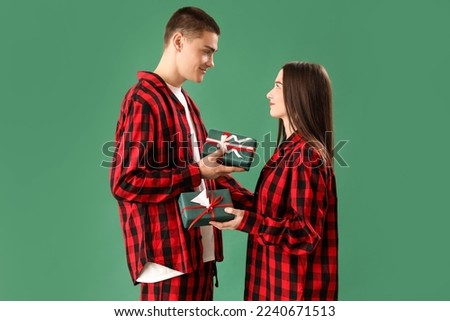 Young couple in pajamas with Christmas gifts on green background