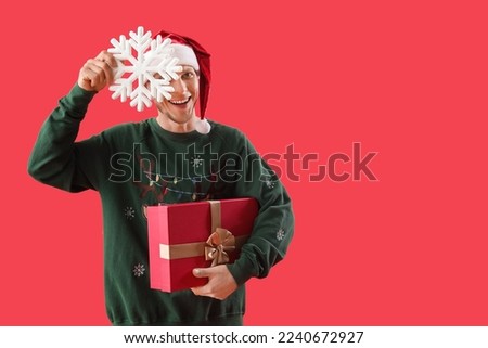 Handsome man in Santa hat with Christmas present and snowflake on red background