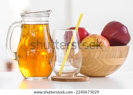 Jug of fresh apple juice, glass and fruits on table in kitchen
