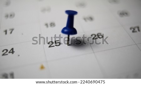 Embroidered blue pins on a calendar on the 25 th  with selective focus Royalty-Free Stock Photo #2240690475