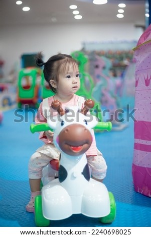 Pretty little kid girl in dress sit on toy at theme park, playing with toys. beautiful baby girl sitting play toys on blur background. Quality picture. concept enjoy holiday.