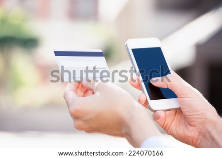 Closeup young woman hands holding credit card and using cell, smart phone for online shopping or reporting lost card, fraudulent transaction, isolated city outside background. New generation gadget