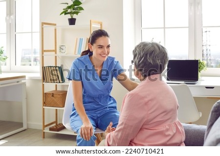 Young doctor giving medical consultation to senior patient. Friendly nurse or physician in blue scrubs looking at old woman, talking to her, trying to support and reassure her