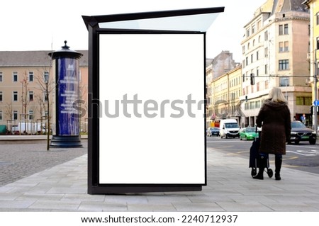bus shelter at busstop. transit station. blank white lightbox. empty billboard. glass and aluminum structure. urban setting. city street background. stone sidewalk. base for mockup. selective focus.