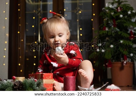 Beautiful little one-year-old girl with blonde hair playing Christmas gifts. Bokeh garlands. Children and new year's eve.