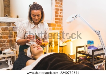 Beautician applying few drops of oily serum onto the face of her female client. SPA day concept. Skincare salon interior. High quality photo
