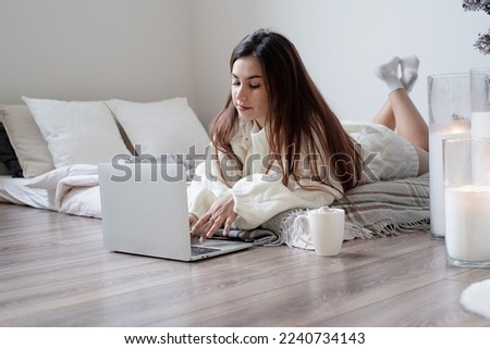 Merry Christmas and Happy New Year. Woman in warm white winter sweater lying in bed at home using laptop, watching movies or working