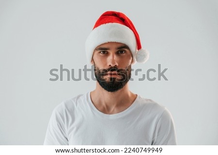 In santa hat. Handsome man is in the studio against white background. Royalty-Free Stock Photo #2240749949