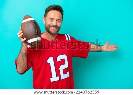Middle age caucasian man playing rugby isolated on blue background extending hands to the side for inviting to come