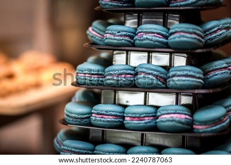 Blue luxurious French macaron desserts piled high on tiered tray in blurred out industrial kitchen setting full of baked pastries in the background