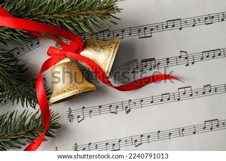 Bells and fir tree branches on music sheet, flat lay. Christmas decor