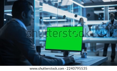 Software Developer Working on Computer with Green Screen Mock Up Display. Scientific Lab, Engineering Research Center with Specialists Working on Turbine Engine Development in the Background.