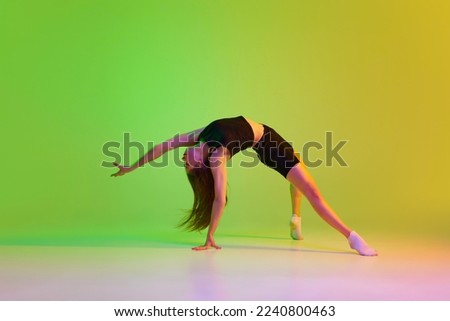 Young sportive girl training over gradient green yellow background in neon light. Flexibility. Youth culture, style and fashion. Concept of dance, youth, hobby, dynamics, movement, action, ad