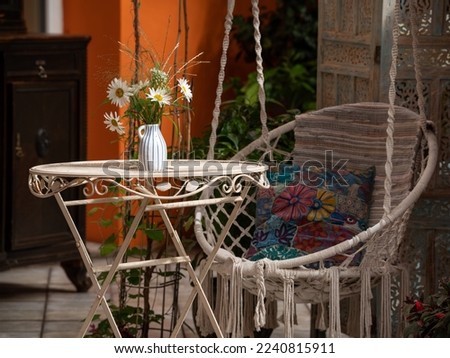 Interior of veranda. Hanging wicker chair, flowers on table. Close-up.